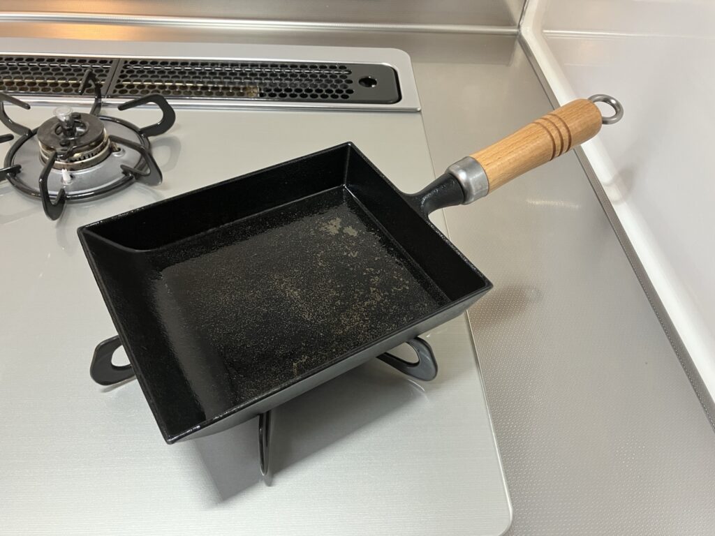 岩鋳の南部鉄器玉子焼（木柄付）をガスコンロに置いた写真。木柄付き