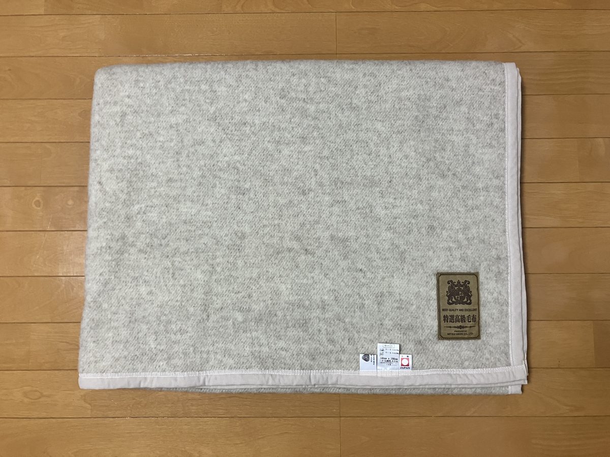 たたんだ状態の三井毛織 無染色ウール毛布 W508E の全体。生成り色の生地と特選高級毛布のブランドタグ